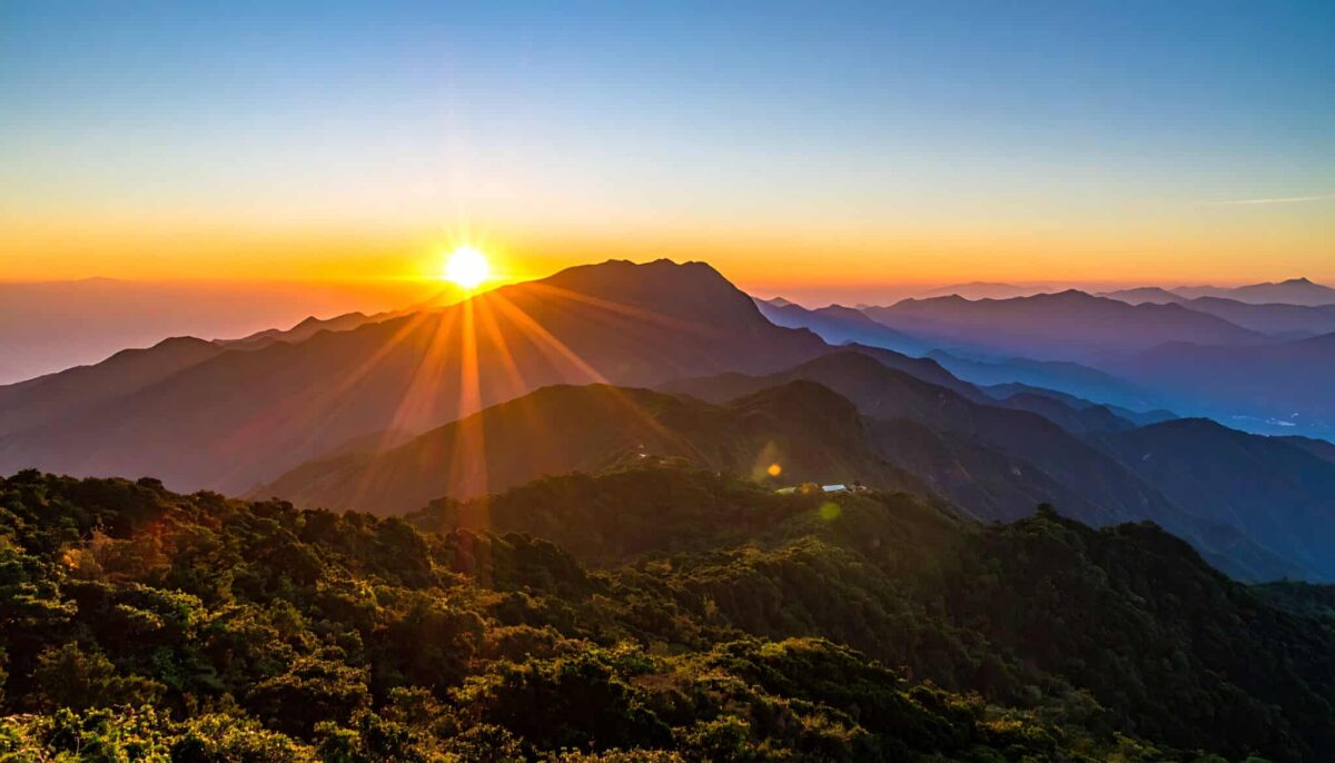 Sunrise over mountainous landscape, sunburst behind peaks, golden light, serene atmosphere, nature beauty
